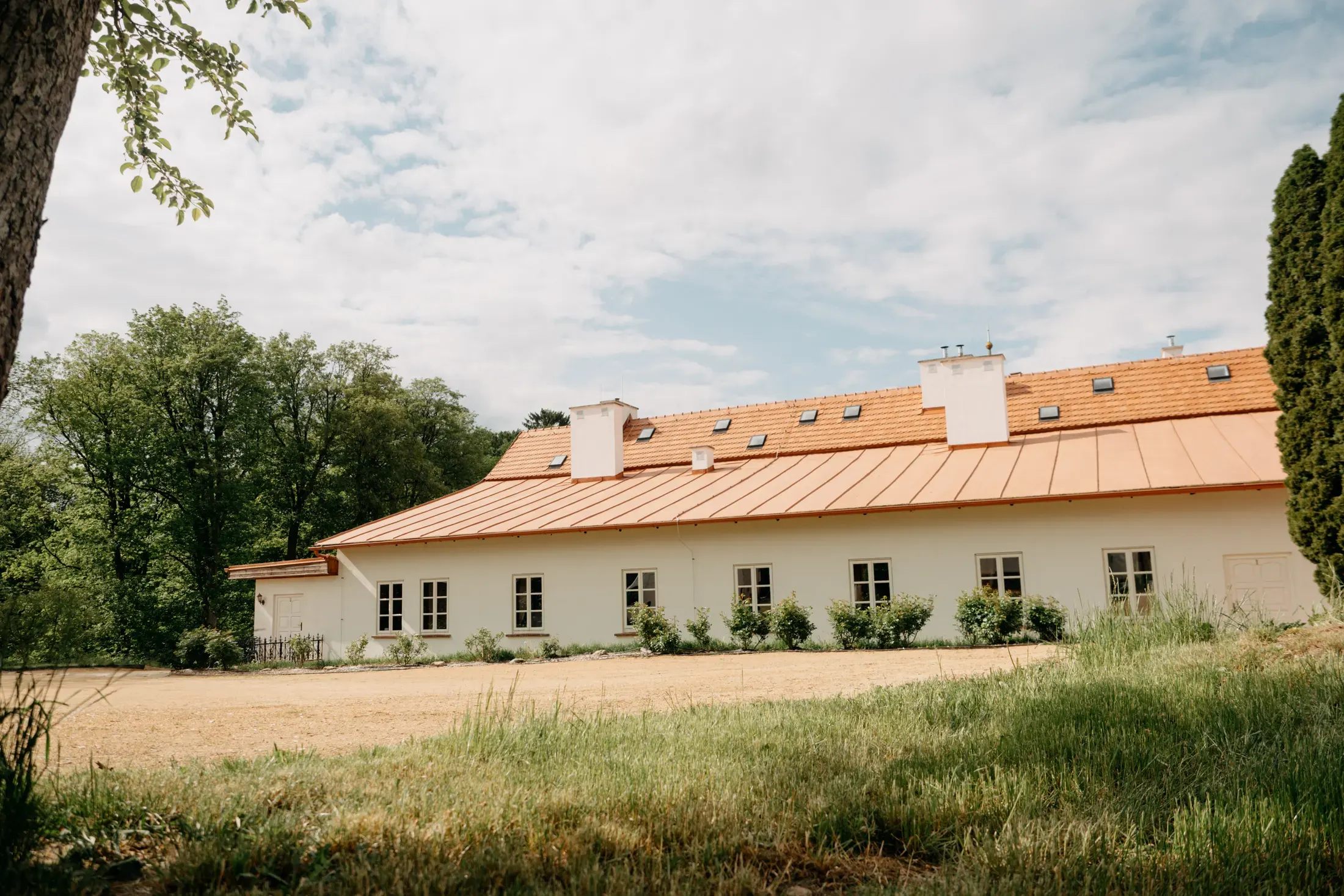 Apartmánové křídlo s měděnou střechou nad loukou.