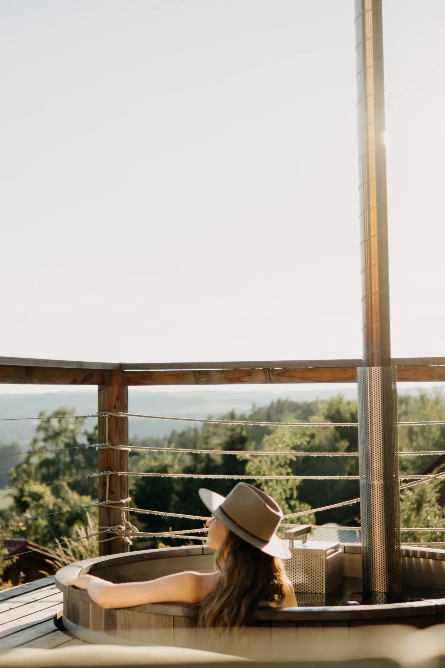 A woman in a hat in the stainless-steel hot tub overlooking the Vysočina landscape.