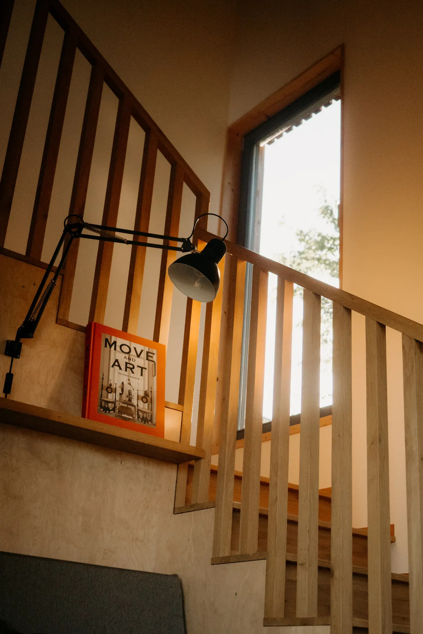 The wooden staircase with a lamp and a book by a tall window.