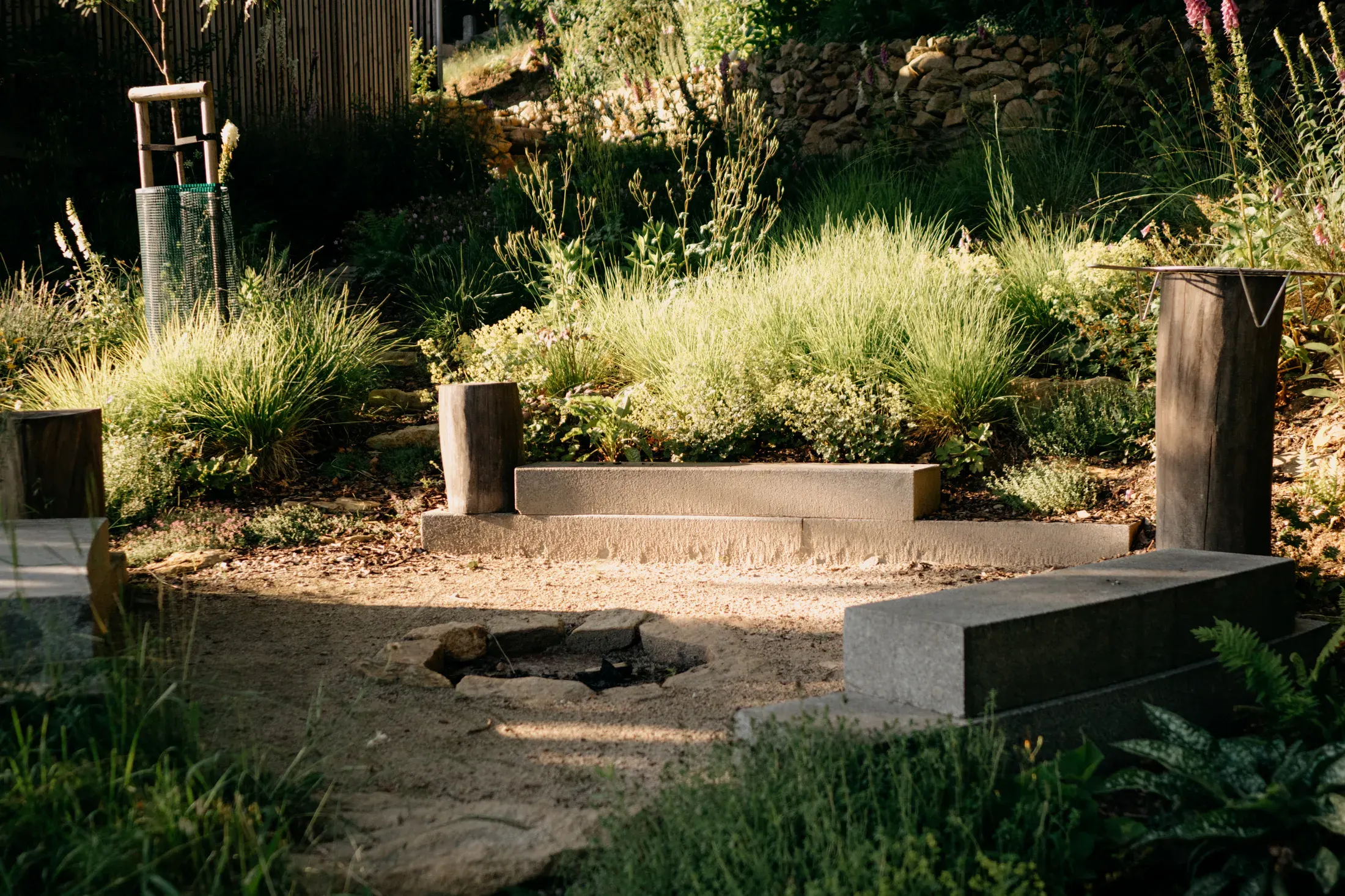 A stone fire pit with seating in the garden among the grasses.