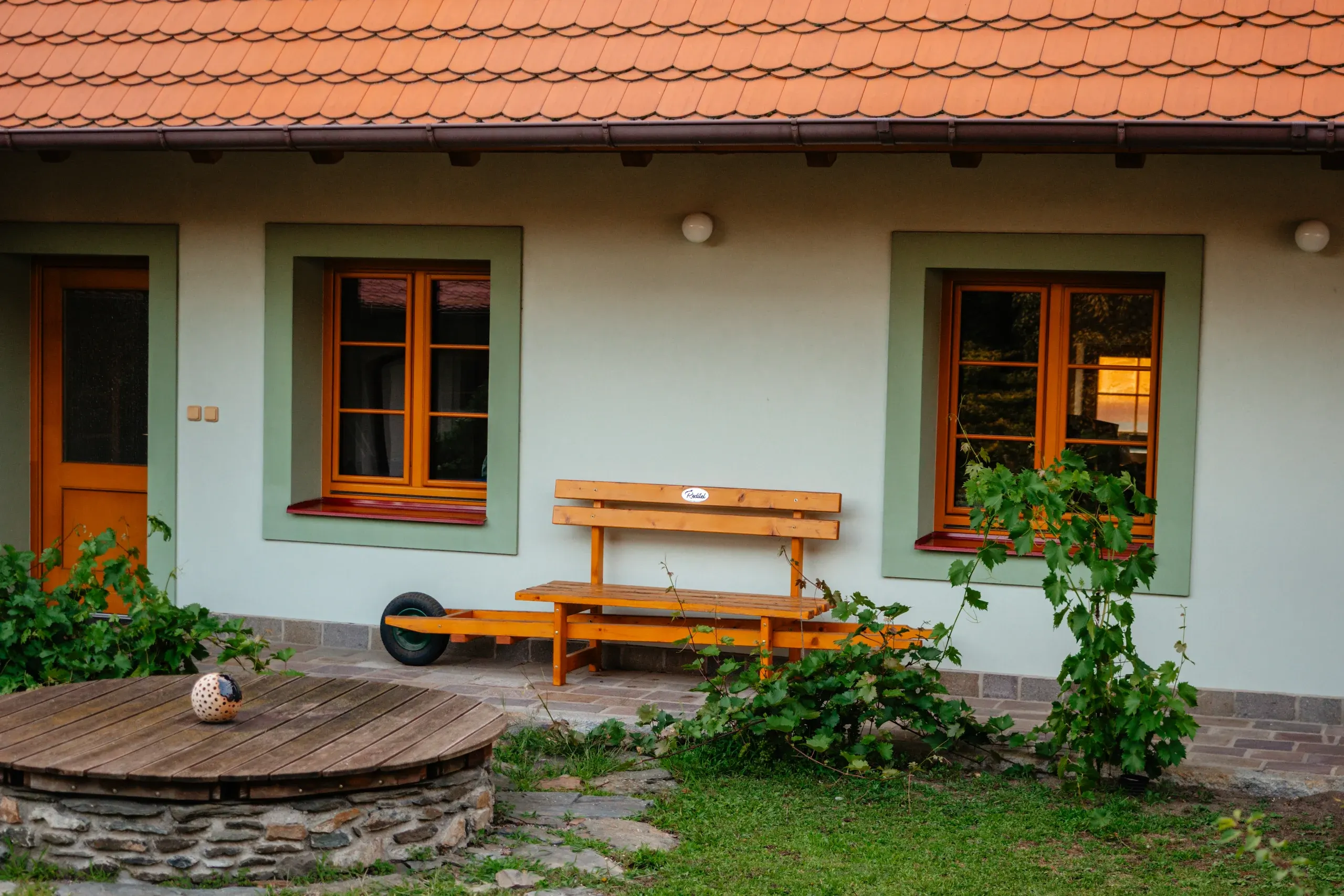Průčelí Besedy s lavičkou a kamennou studnou na zahradě.