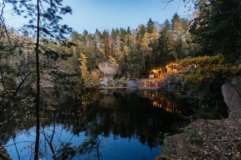 The flooded quarry ringed by rocks and autumn forest, the floating sauna in the distance.