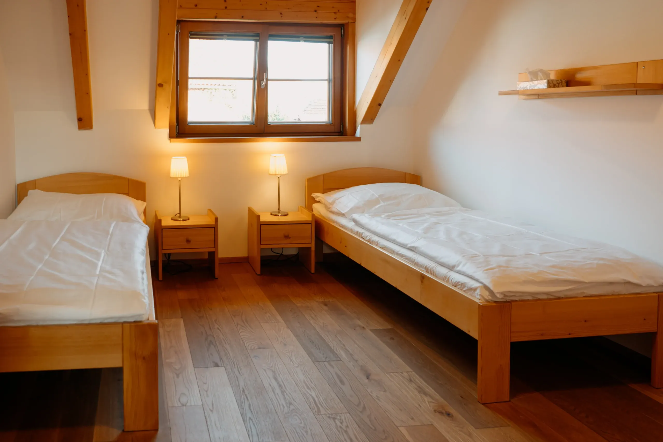 Podkrovní pokoj v Besedě se dvěma lůžky a nočními lampami.