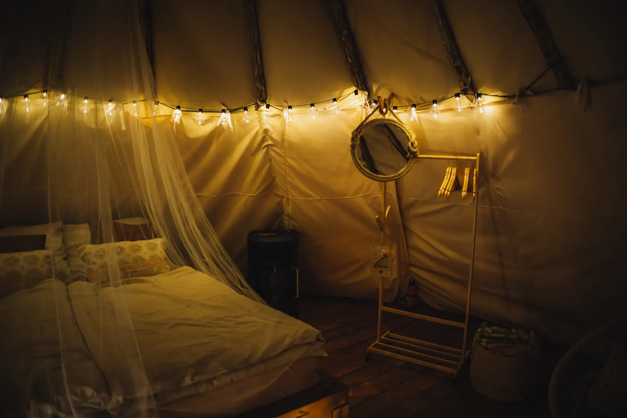 Večerní atmosféra v teepee, girlandy světel nad postelí.